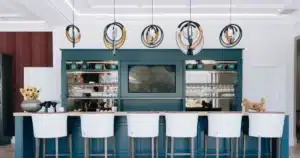 Modern Gesture handcrafted circular pendant lights suspended above a deep teal kitchen island and bar with white stools.